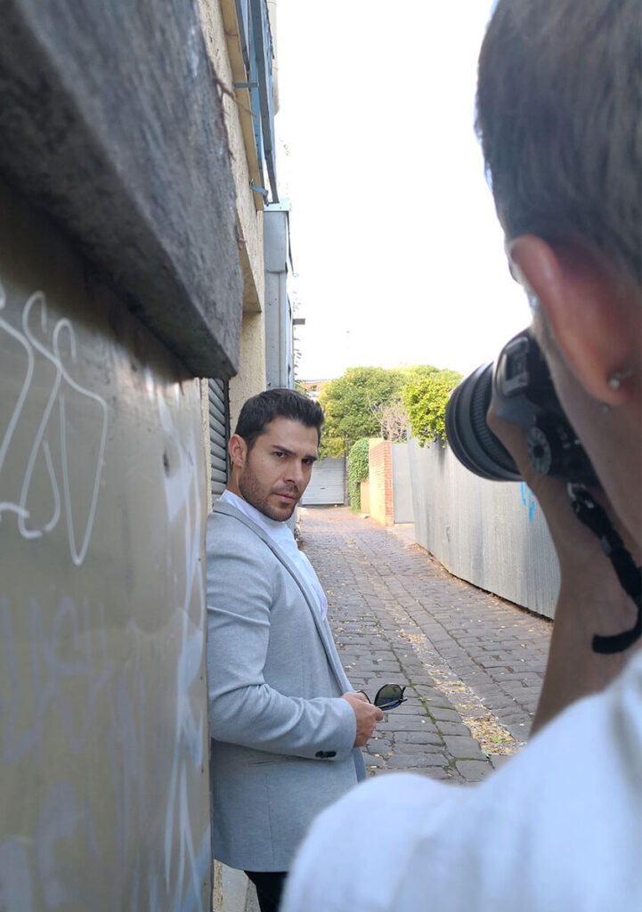 A man wearing grey colour blazer is looking side ways towards a photographer holding a Nikon camera.